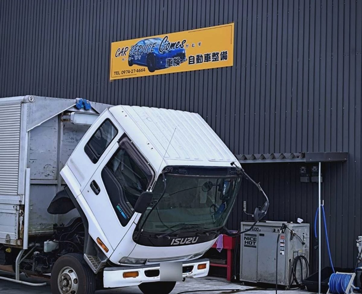 カムズの看板の前で、キャブを起こして整備中の大型トラック